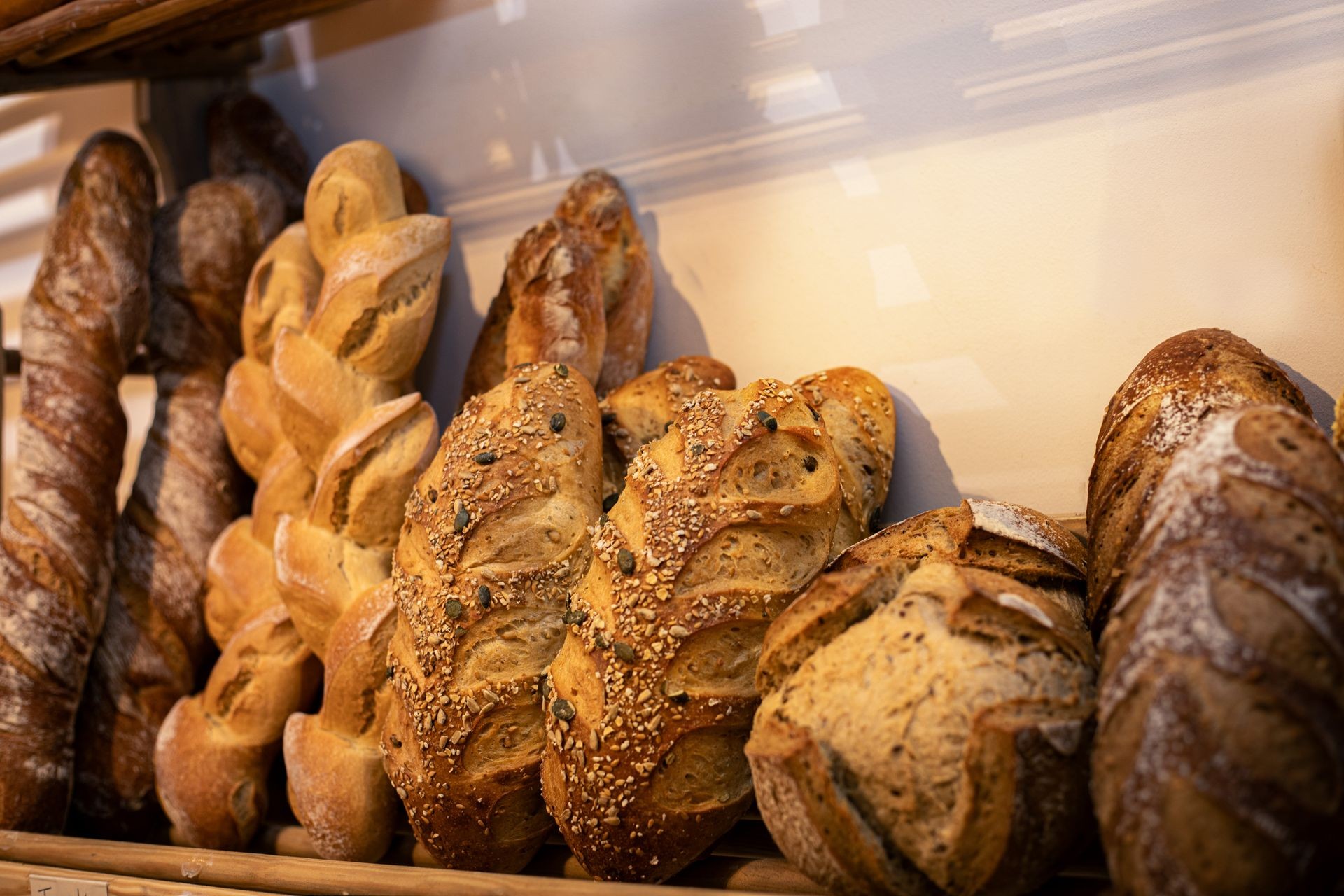 An assortment of artisan bread loaves displayed on a shelf, including seeded and crusty varieties.